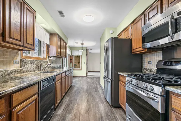 a kitchen with stainless steel appliances granite countertop a stove top oven a sink dishwasher a refrigerator and cabinets with wooden floor