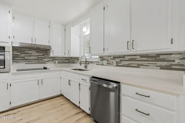 a kitchen with stainless steel appliances granite countertop a stove a sink and white cabinets with wooden floor