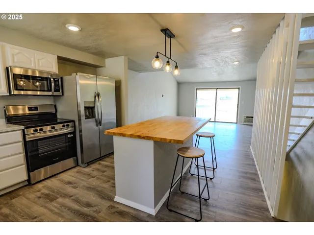a kitchen with stainless steel appliances kitchen island granite countertop a refrigerator a stove a sink dishwasher and a microwave with wooden floor