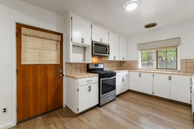 a kitchen with granite countertop wooden floors stainless steel appliances and sink