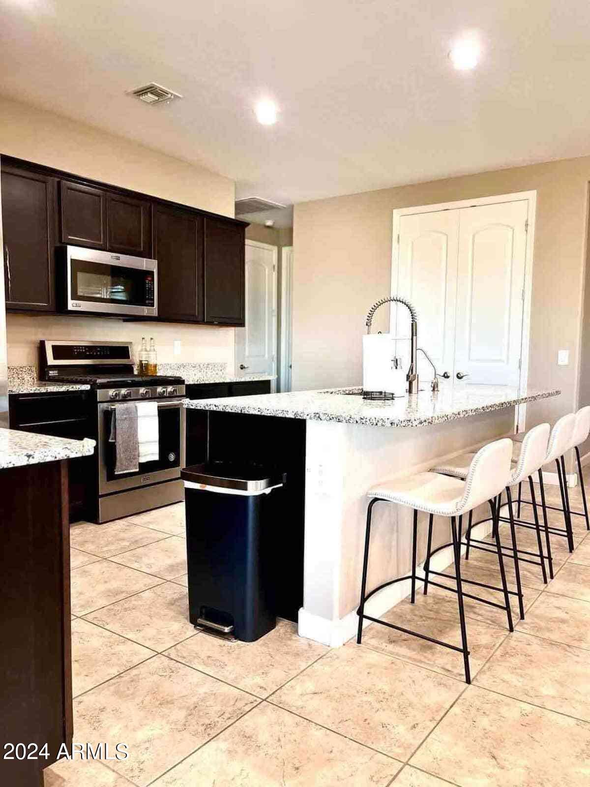 18735 North Ravello Road Maricopa, AZ 85138 - Photo 46 of 50 a kitchen with stainless steel appliances kitchen island granite countertop a stove top oven a sink a dining table and chairs