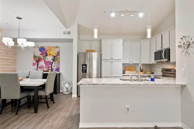 a kitchen with stainless steel appliances granite countertop a refrigerator a stove a sink a dining table and chairs with wooden floor