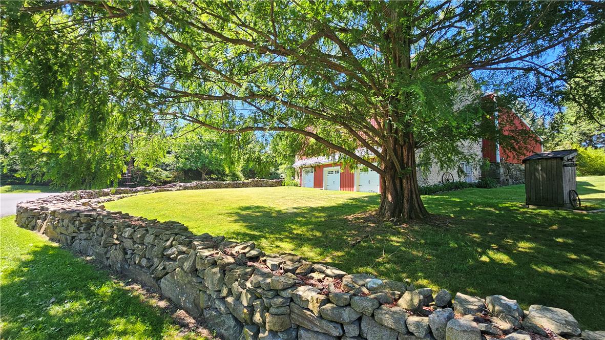 585 Buttermilk Road Hellertown, PA 18055 - Photo 63 of 82 Mature trees and a stone wall delineate this charming, verdant property, featuring a red barn in the background.