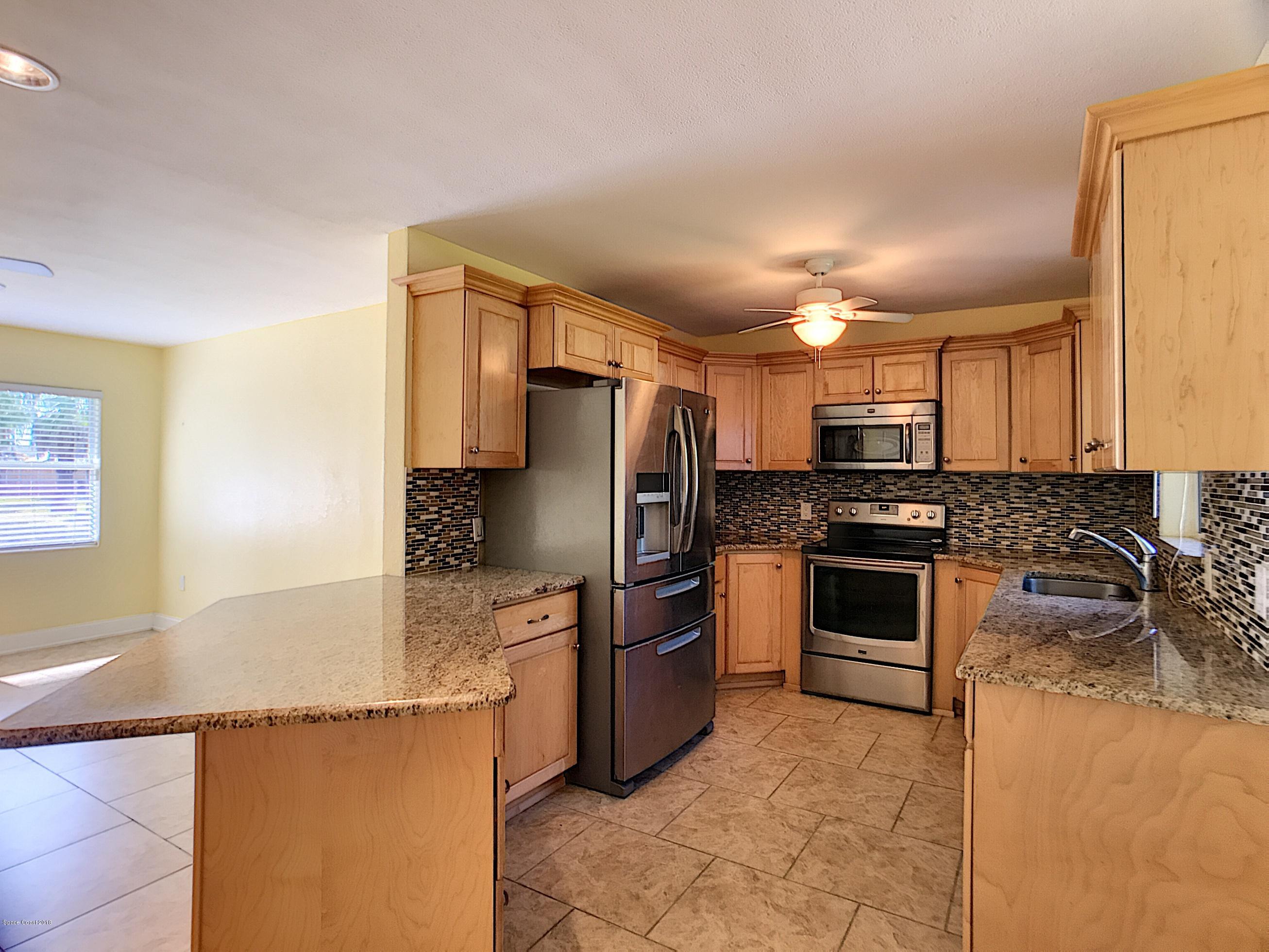 327 3rd Street Merritt Island, FL 32953 - Photo 4 of 26 a kitchen with granite countertop a refrigerator and a stove top oven