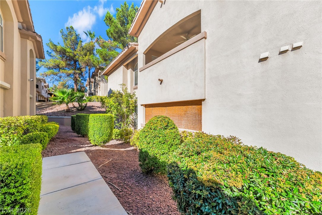 2050 West Warm Springs Road, Unit 2411 Henderson, NV 89014 - Photo 32 of 37 Manicured hedges border a concrete path leading to a stucco building with a charming balcony.