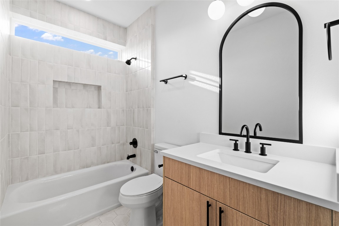 2950 Pitzlin Street Houston, TX 77023 - Photo 18 of 37 A crisp, modern retreat—this bathroom pairs soft, vertical tilework with bold matte black finishes and warm wood cabinetry. A sleek arched mirror, built-in shower niche, and clerestory window add architectural elegance while filling the space with natural light.