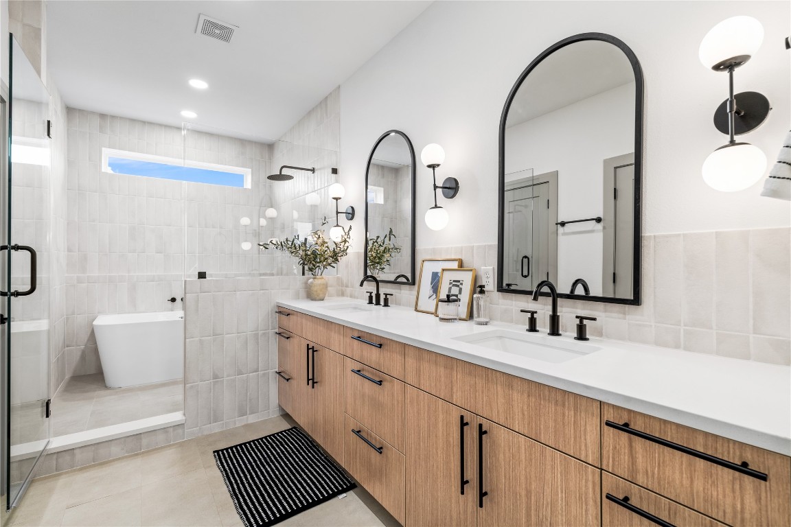 2950 Pitzlin Street Houston, TX 77023 - Photo 24 of 37 This spa-like primary bathroom blends contemporary luxury with timeless design—featuring a floating dual vanity with quartz counters, arched mirrors, matte black fixtures, and a frameless glass shower. A soaking tub tucked beneath a picture window completes the retreat, offering a perfect place to unwind in style.