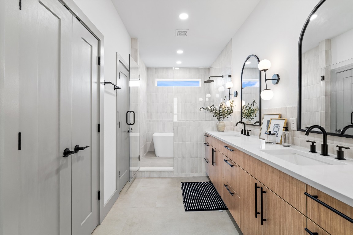 2950 Pitzlin Street Houston, TX 77023 - Photo 25 of 37 With a layout designed for ease and indulgence, this primary bathroom combines luxury and functionality—featuring a double vanity with quartz counters, matte black fixtures, and ample storage. A glass-enclosed shower and freestanding tub sit beneath a clerestory window, bathing the space in soft natural light for a spa-like experience every day.