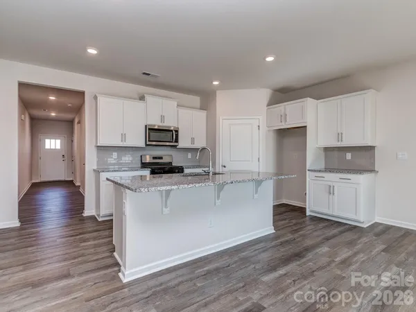 a kitchen with stainless steel appliances granite countertop a stove a sink a refrigerator and white cabinets