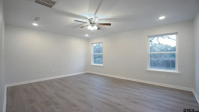 an empty room with wooden floor fan and windows