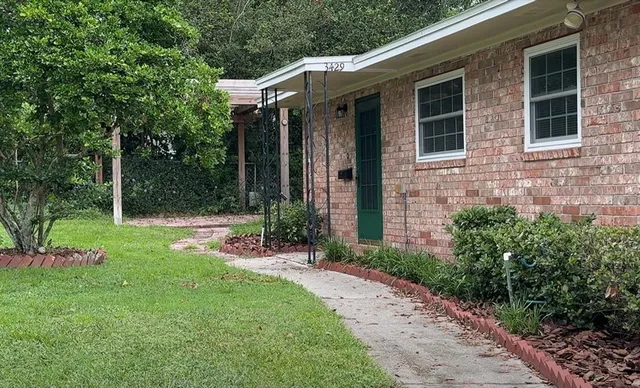 a view of brick house with a yard and large tree