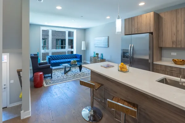 a room with stainless steel appliances kitchen island granite countertop a refrigerator a sink dishwasher a dining table and chairs with wooden floor