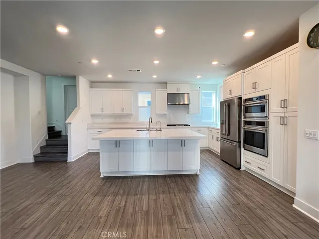 a large kitchen with stainless steel appliances a large counter top a stove and a wooden floors