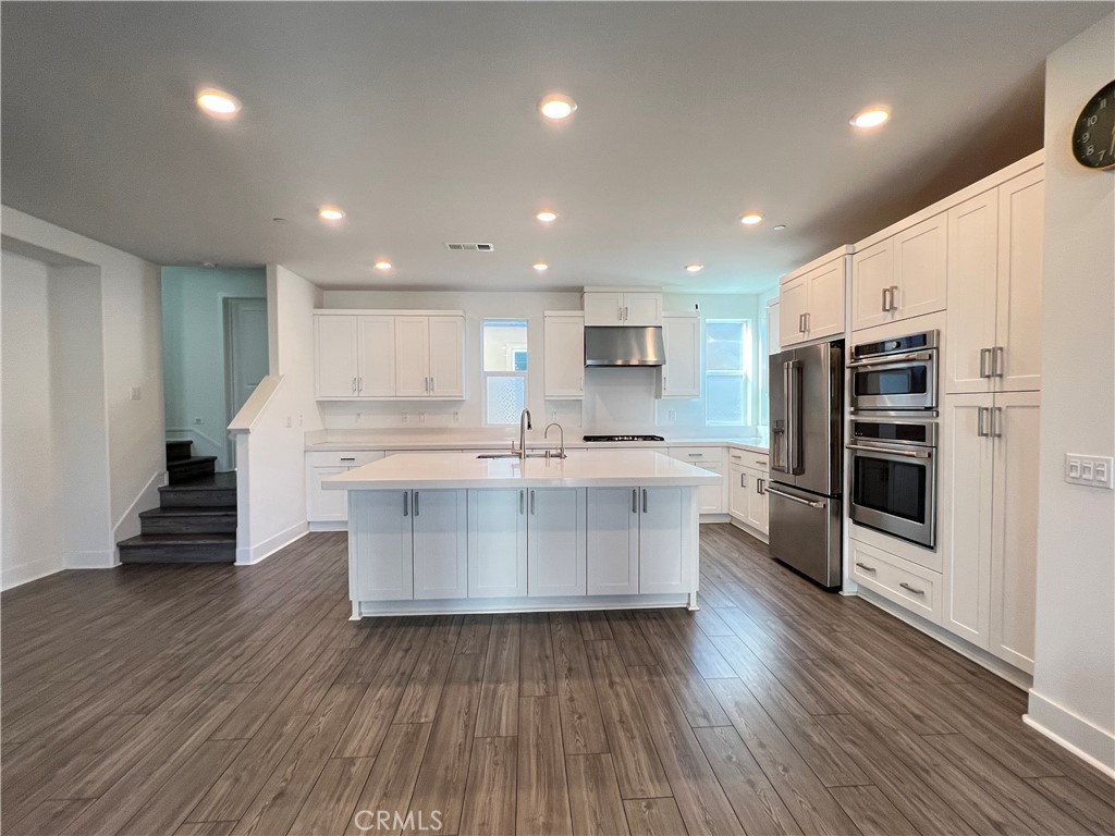 a large kitchen with stainless steel appliances a large counter top a stove and a wooden floors