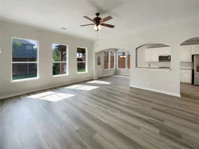 an empty room with wooden floor a ceiling fan a fireplace and windows