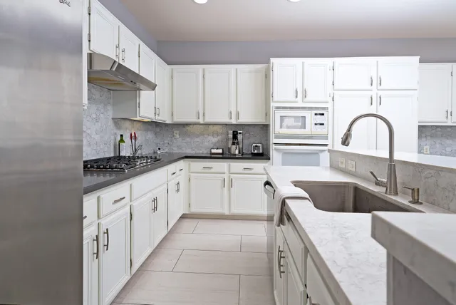 a kitchen with granite countertop a sink white cabinets and stainless steel appliances