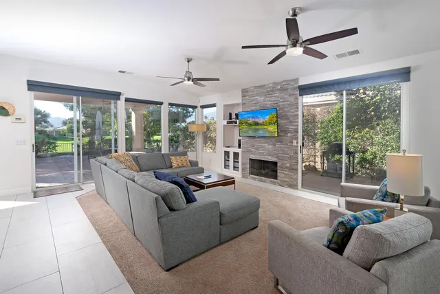 a living room with furniture a ceiling fan a fireplace and a large window