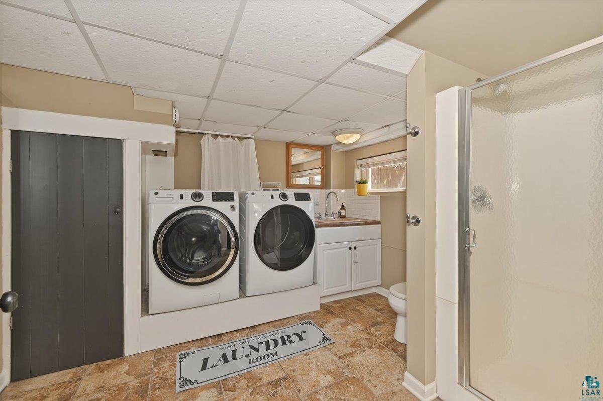 1918 West Kent Road Duluth, MN 55812 - Photo 26 of 42 Dedicated laundry area featuring side-by-side front-loading machines, a utility sink with a wood-finish countertop, white cabinetry, and a white tiled backsplash