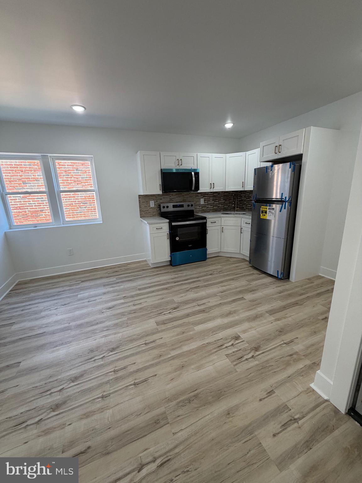 an empty room with wooden floor kitchen view and a window