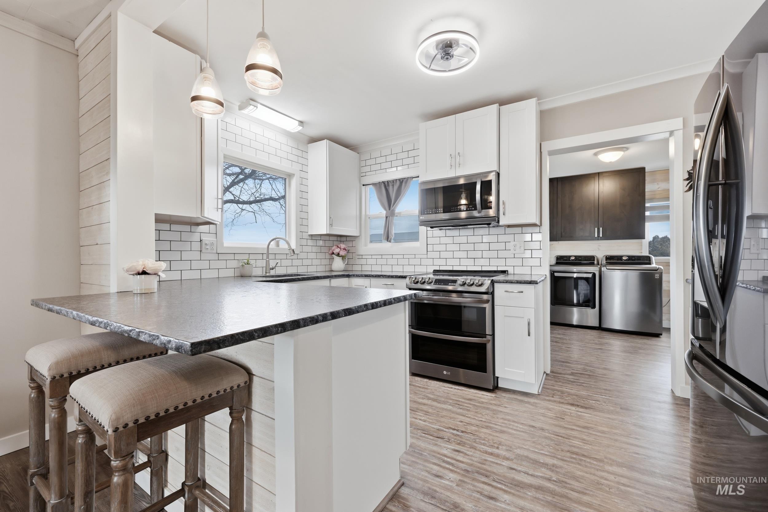 9762 Deer Flat Road Nampa, ID 83686 - Photo 3 of 24 Kitchen with a peninsula, a kitchen breakfast bar, white cabinets, stainless steel appliances, and decorative light fixtures