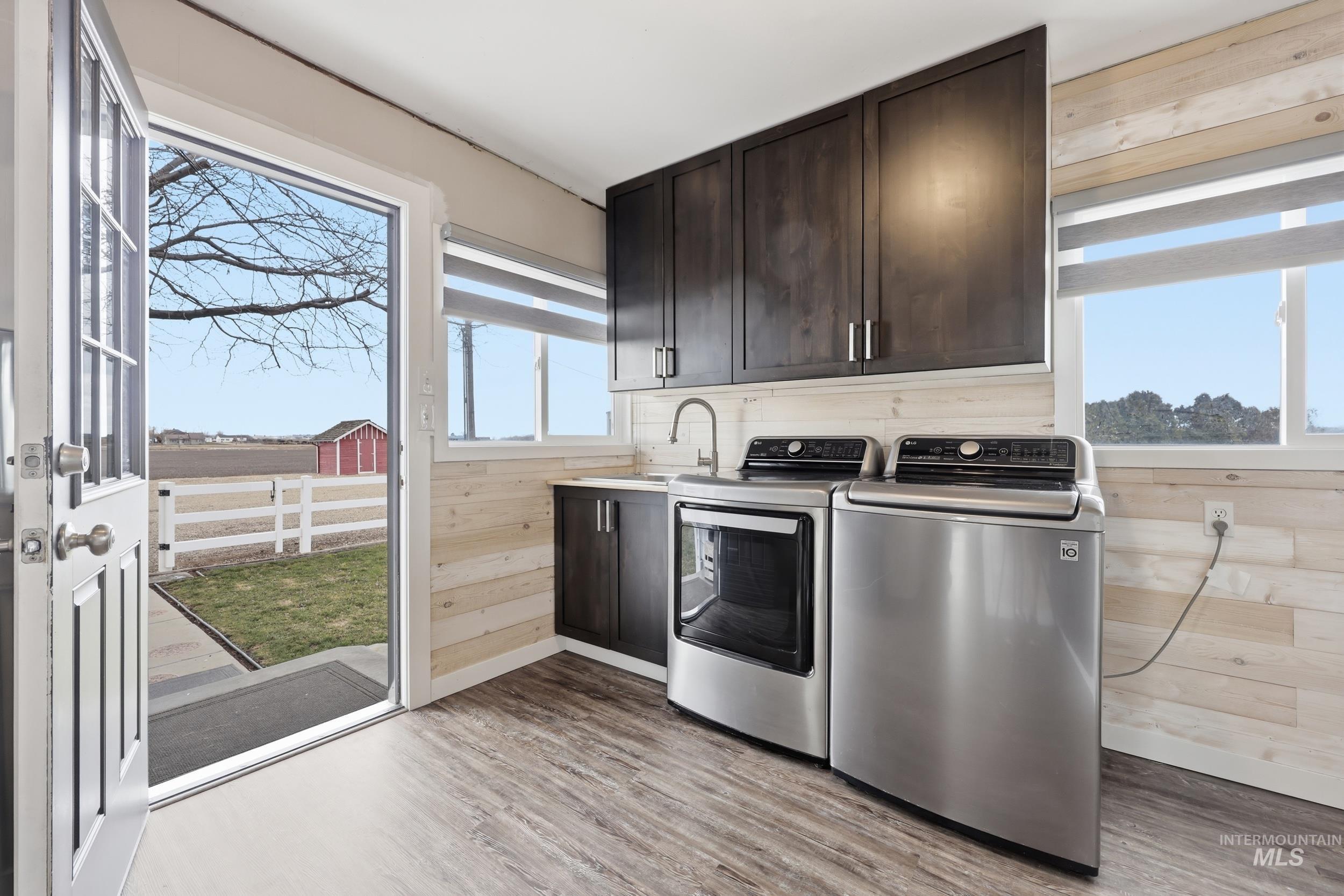 9762 Deer Flat Road Nampa, ID 83686 - Photo 7 of 24 Laundry room with wooden walls, washer and clothes dryer, light wood-style flooring, and cabinet space