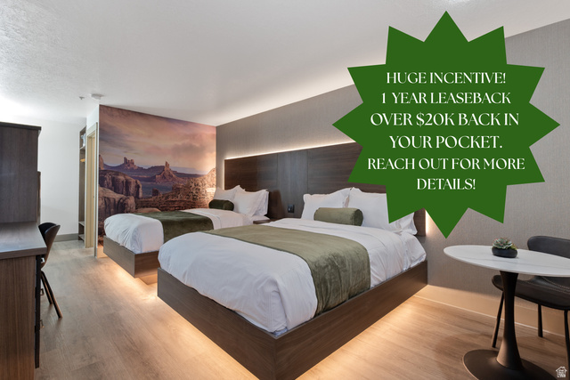 Wood-finish flooring throughout, featuring two platform beds with under-bed lighting, a built-in headboard with integrated lighting, and a prominent desert landscape accent wall