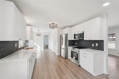 a kitchen with granite countertop a refrigerator a stove and white cabinets with wooden floor