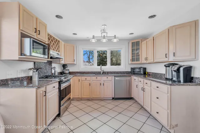 a kitchen with granite countertop white cabinets a sink dishwasher and a stove with wooden floor