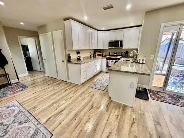 a kitchen with stainless steel appliances a stove top oven a sink a refrigerator white cabinets and wooden floor