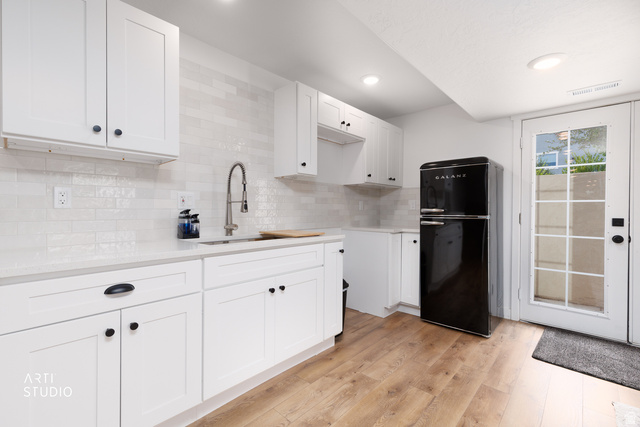 1654 South 730 West Provo, UT 84601 - Photo 23 of 33 Modern kitchen featuring white shaker cabinetry, light-toned countertops, a white subway tile backsplash, wood-finish flooring, and a glass-paned exterior door
