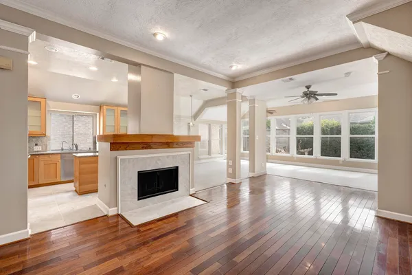 a view of an empty room with wooden floor and a kitchen