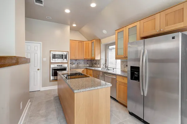 a kitchen with granite countertop stainless steel appliances a refrigerator a stove top oven and sink
