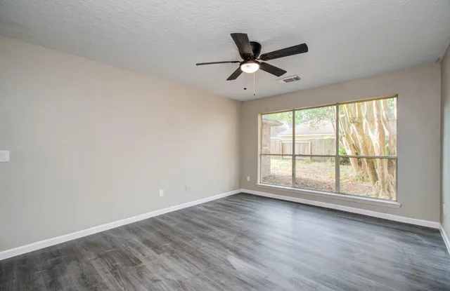 an empty room with wooden floor fan and windows