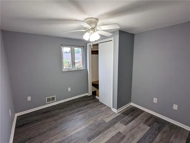 an empty room with wooden floor chandelier fan and windows