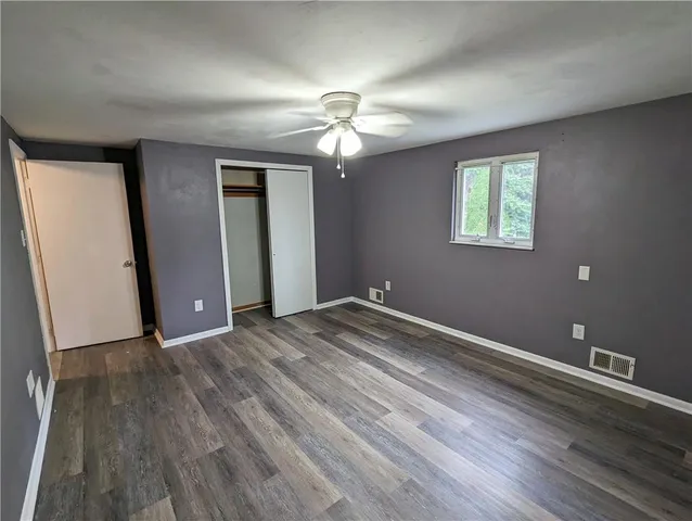 an empty room with wooden floor chandelier fan and windows