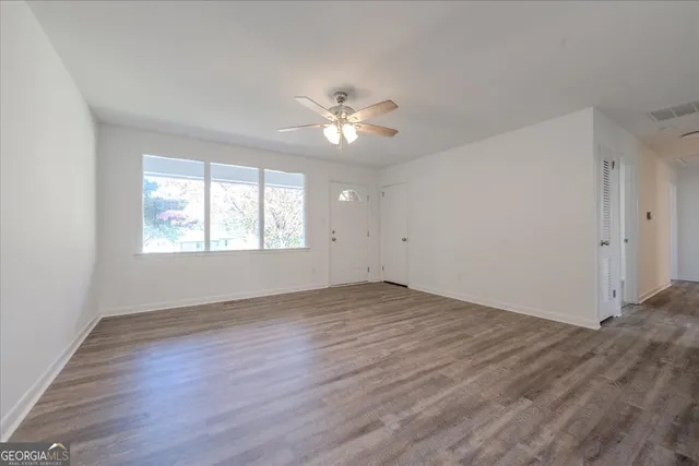 an empty room with wooden floor chandelier fan and windows
