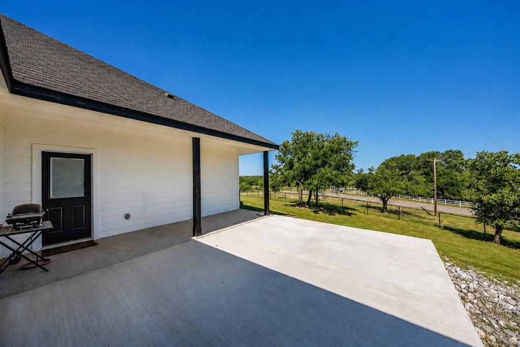 117 Rock Salt Drive Springtown, TX 76082 - Photo 32 of 38 Expansive concrete patio with covered area, white horizontal siding, dark asphalt shingle roof, and black trim details
