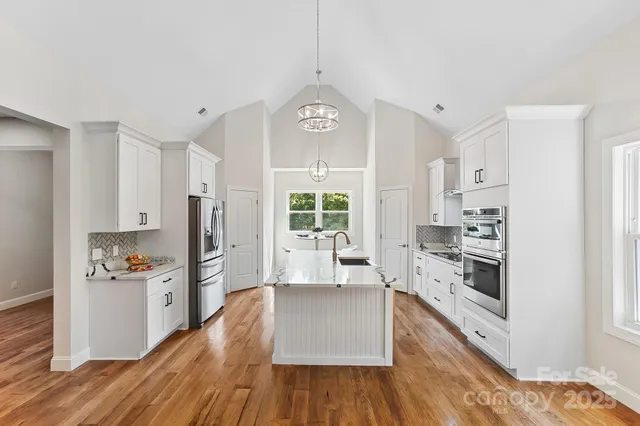 a kitchen with stainless steel appliances a stove a sink a refrigerator cabinets and wooden floor