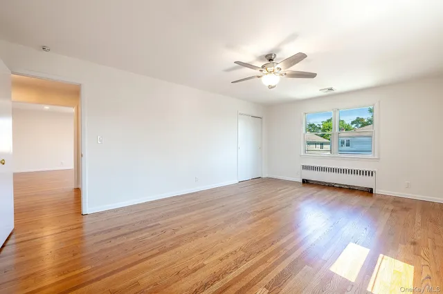 an empty room with wooden floor chandelier fan and windows