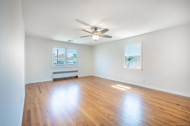 an empty room with wooden floor chandelier fan and windows