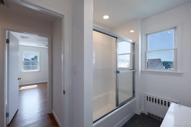 a view of a hallway with wooden floor and a bathroom