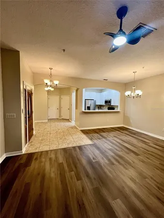 a view of a room with wooden floor a ceiling fan and kitchen view