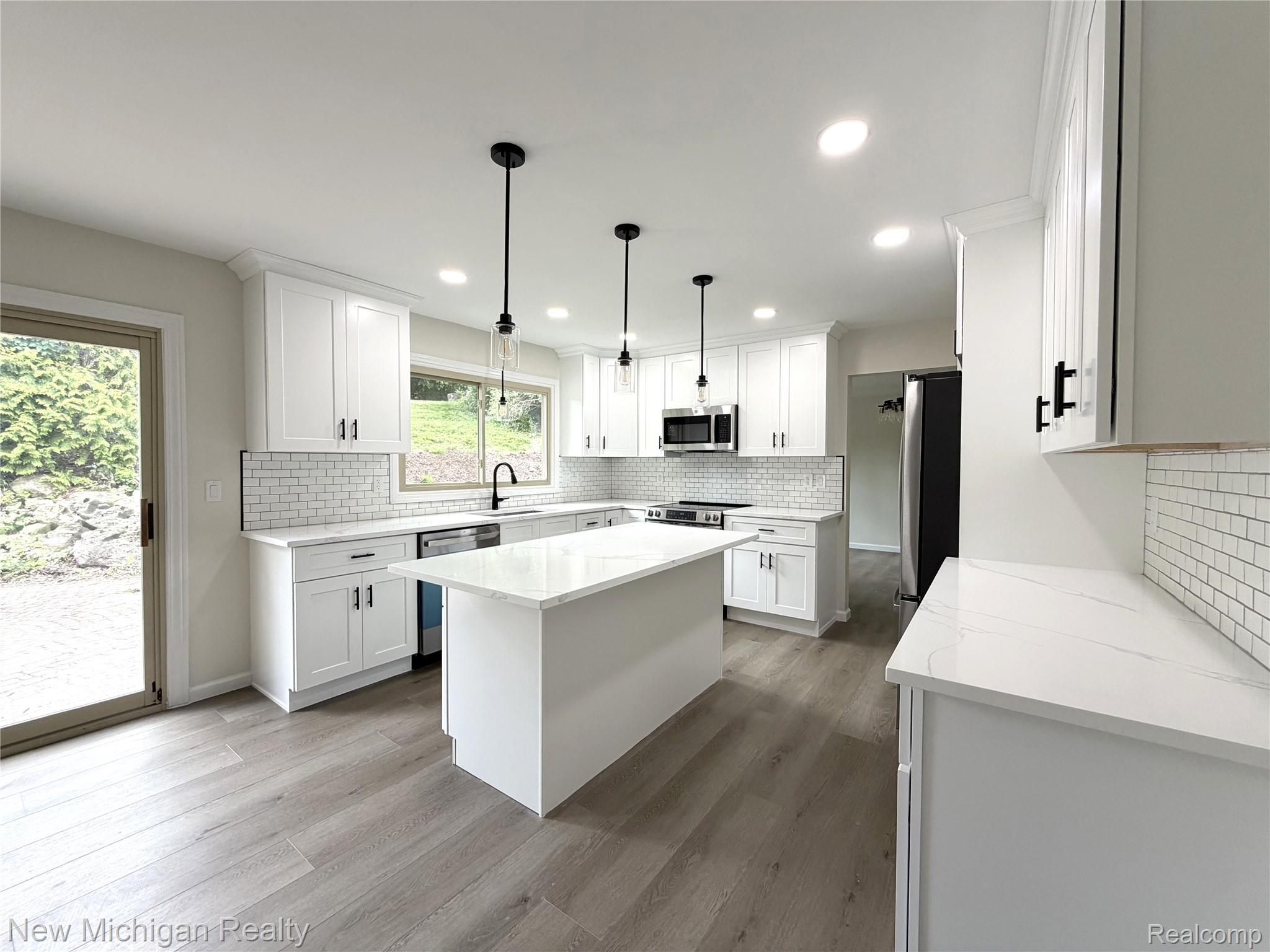 Bright kitchen featuring white cabinetry, quartz countertops, subway tile backsplash, and a central island