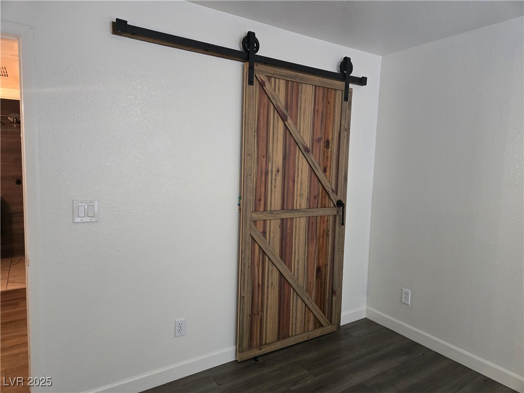 3168 Tarpon, Unit 103 Las Vegas, NV 89120 - Photo 12 of 23 Unfurnished bedroom featuring dark wood-style flooring and a barn door