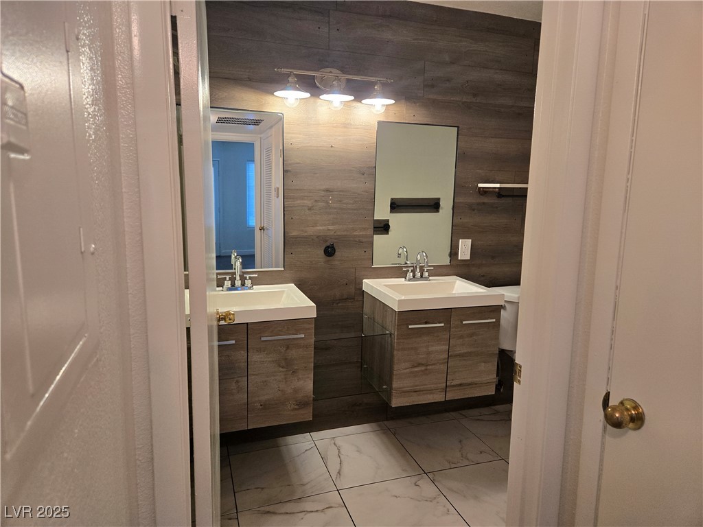 3168 Tarpon, Unit 103 Las Vegas, NV 89120 - Photo 14 of 23 Bathroom with wooden walls, two vanities, and light marble finish floors