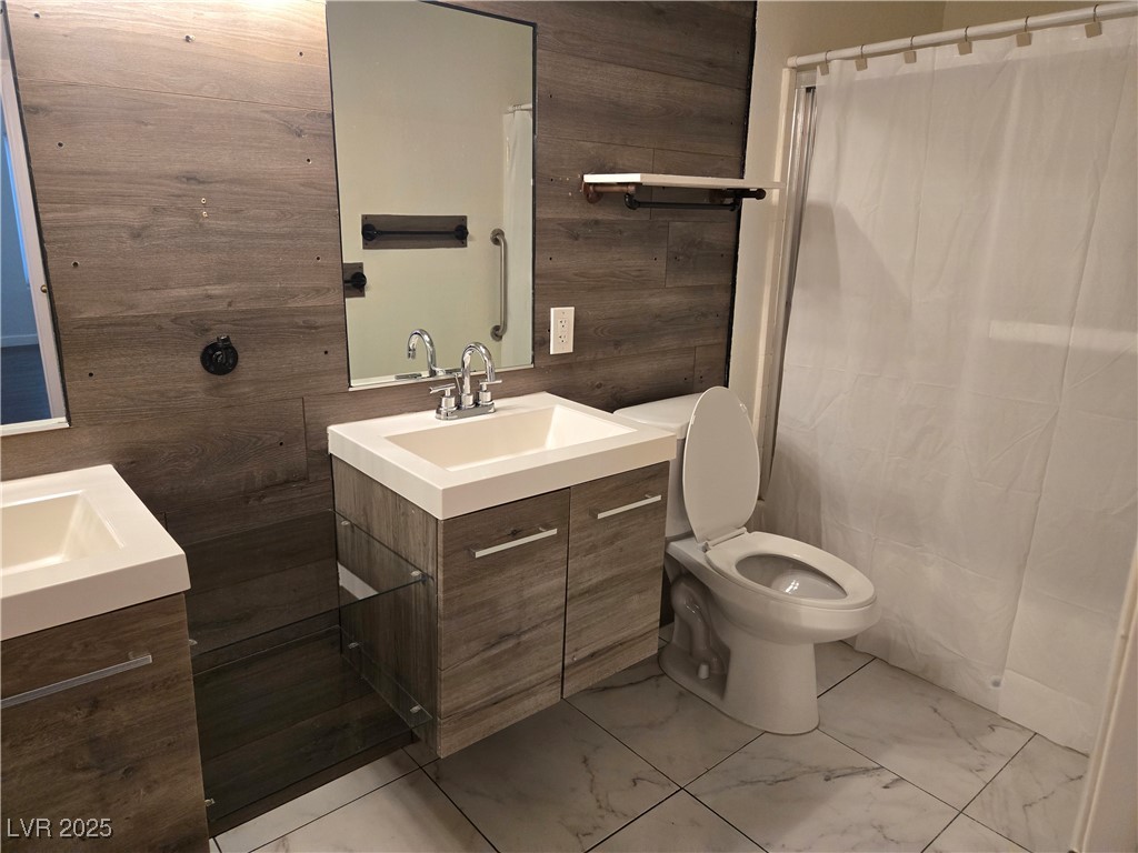 3168 Tarpon, Unit 103 Las Vegas, NV 89120 - Photo 15 of 23 Bathroom featuring two vanities, wood walls, a shower with curtain, and light marble finish floors