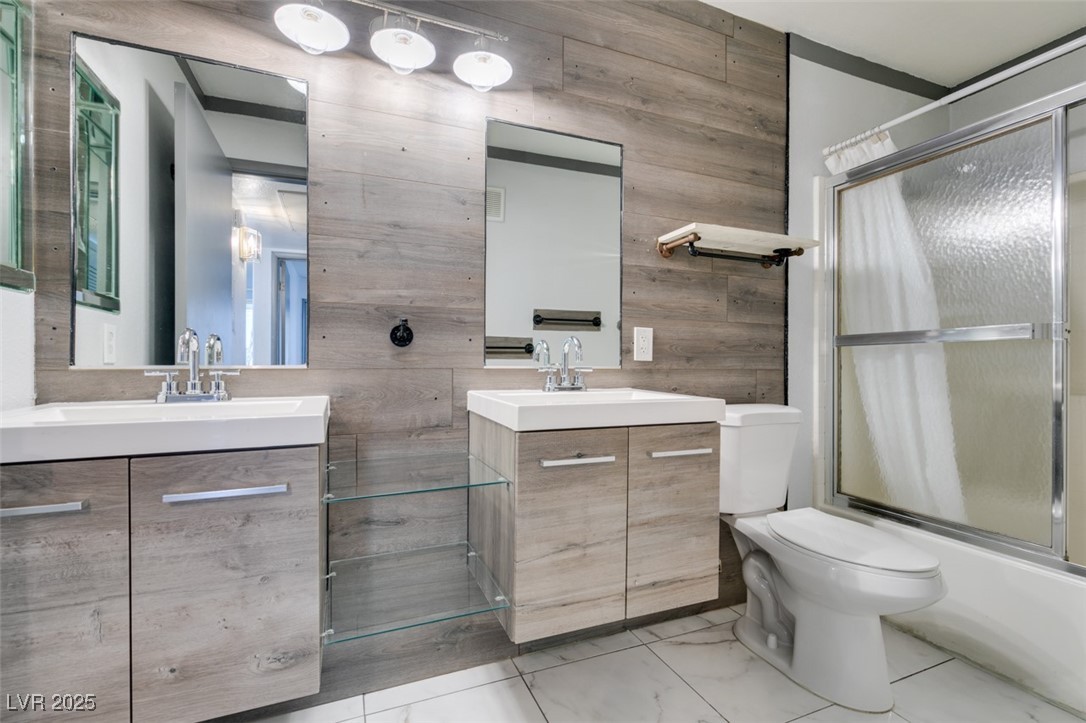 3168 Tarpon, Unit 103 Las Vegas, NV 89120 - Photo 19 of 23 Bathroom with two vanities, wood walls, and combined bath / shower with glass door