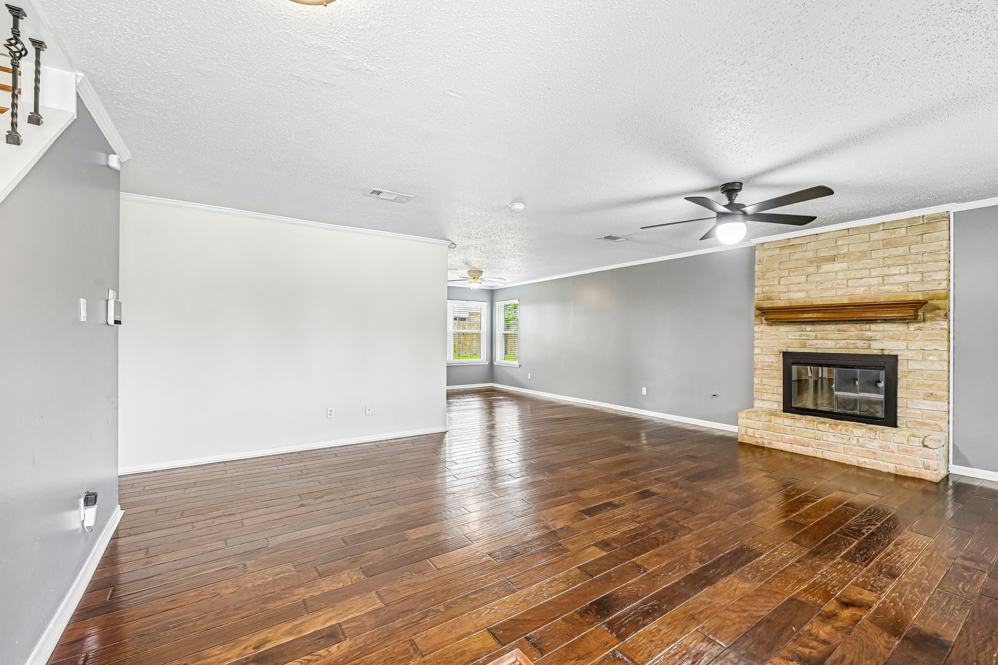8 Arlington Street Conroe, TX 77301 - Photo 11 of 37 Spacious living area with rich hardwood floors, neutral walls, and a brick fireplace. Ceiling fan adds comfort, and a large windows provides natural light. Ideal for cozy gatherings.
