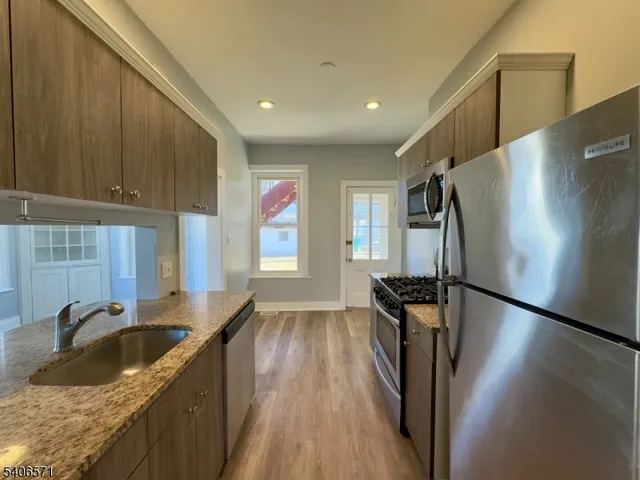 a kitchen with granite countertop a refrigerator a sink a stove and cabinets