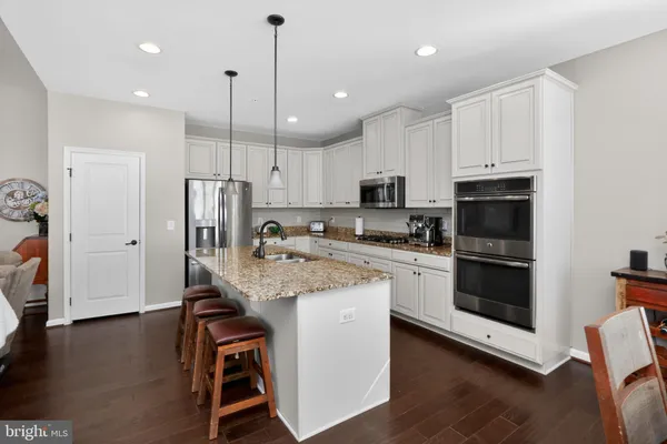 a kitchen with stainless steel appliances granite countertop a sink a stove a refrigerator and white cabinets with wooden floor